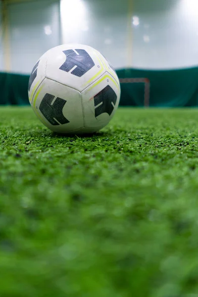 A black and white soccer ball lies on a sports field on a green synthetic grass before the start of sports game close-up