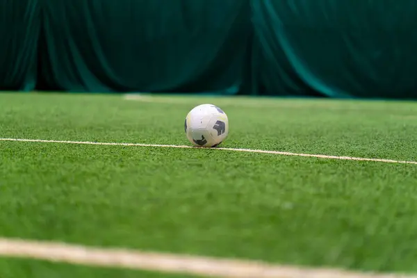 A black and white soccer ball lies on a sports field on a green synthetic grass before the start of sports game