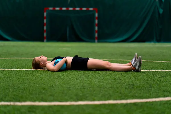 women\'s soccer tired female soccer player lying resting green synthetic grass field after hard training or match