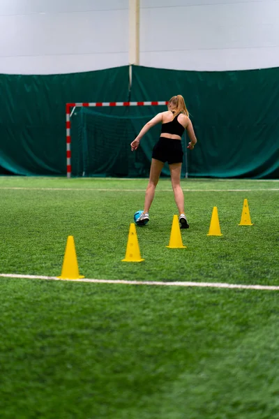 若い女の子は試合のために準備するチップまたはコーンの間でボールを運転するサッカー場で訓練しています — ストック写真