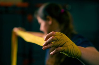 Güçlü kolları olan sportif kız sıkı bir idmana hazırlanıyor. Yumruklarını bandajla sarıyor. Parmaklarını jimnastik salonunda koruyor.