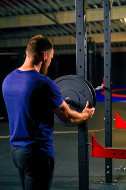 Spor salonundaki halterlere ağırlık ekleyen erkek sporcu vücut geliştiricinin üzerindeki yükü artırır.