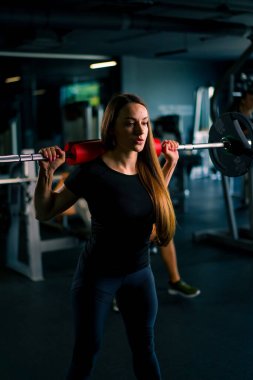 Konsantre bir fitness kadınının portresi. Spor salonunda halterle ağırlık çalışması yapıyor. Kas gruplarında.