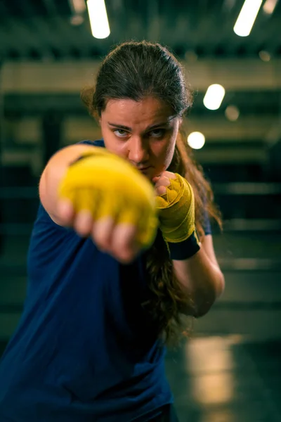 肖像画は戦いの前にジムの暗い背景のボクシングスタンスに立っている黄色いボクシング包帯のボクサーの少女を焦点にしました — ストック写真
