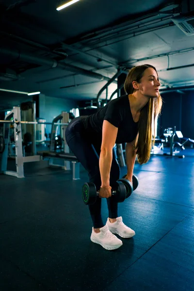 集中フィットネス女性トレーナーは ジムトレーニングボディービルの競争で筋肉をポンプで手でダンベルでエクササイズを行います — ストック写真