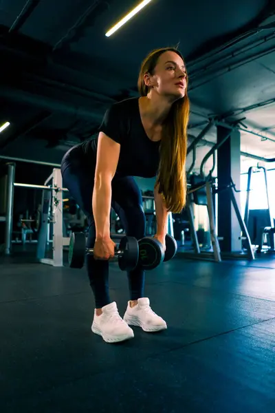 集中フィットネス女性トレーナーは ジムトレーニングボディービルの競争で筋肉をポンプで手でダンベルでエクササイズを行います — ストック写真