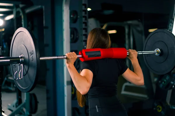concentrated fitness woman doing heavy shoulder press exercise with barbell gym training muscle group back view