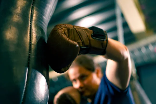 a girl boxer in gloves works out the strength of punches on a punching bag in the gym trains hard before fight close-up