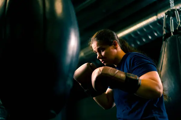 a girl boxer in gloves works out the power of punches on a punching bag in the gym trains hard before fight