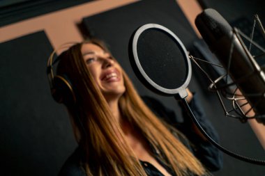 Yeni bir şarkı yaratmak için kayıt stüdyosunda mikrofon önünde kulaklık takan bir kız şarkıcının yakın çekimi.