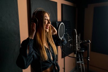 Yeni bir şarkı yaratmak için bir kayıt stüdyosunda mikrofon başında şarkı söyleyen bir kız.