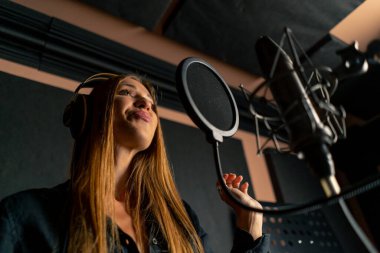 Yeni bir şarkı yaratmak için bir kayıt stüdyosunda mikrofon başında şarkı söyleyen bir kız.