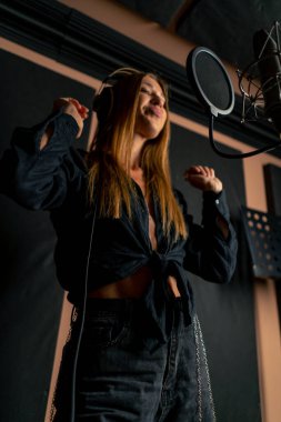 Yeni bir şarkı yaratmak için bir kayıt stüdyosunda mikrofon başında şarkı söyleyen bir kız.