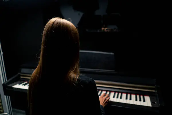 長髪の少女作曲家がカメラの背中に座り レコーディングスタジオでピアノを演奏する — ストック写真