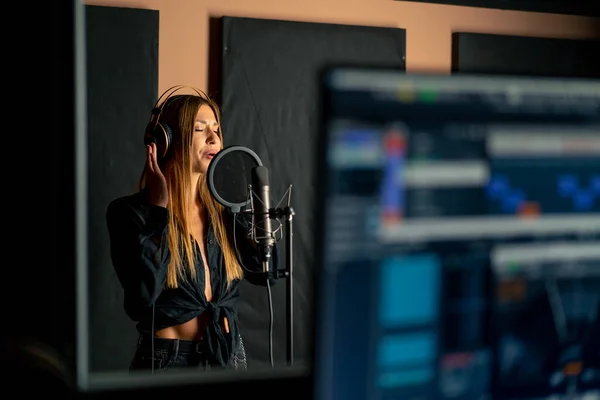 girl singer singing in a recording studio with headphones in front of a microphone to create a new song