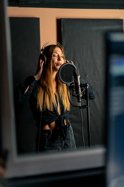 girl singer singing in a recording studio with headphones in front of a microphone to create a new song