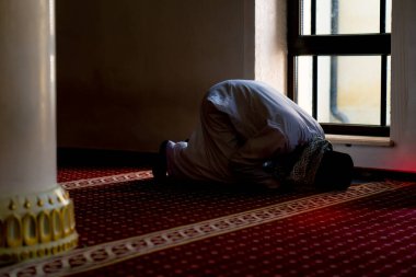 Ulusal giysilere inanan bir inanan camiinin penceresinin yanındaki alacakaranlıkta dua eder ve Allah 'a döner.