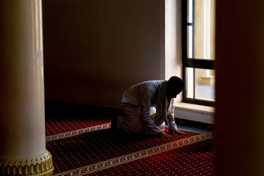 Ulusal giysilere inanan bir inanan camiinin penceresinin yanındaki alacakaranlıkta dua eder ve Allah 'a döner.
