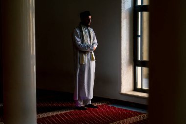 Ulusal giysilere inanan bir inanan camiinin penceresinin yanındaki alacakaranlıkta dua eder ve Allah 'a döner.