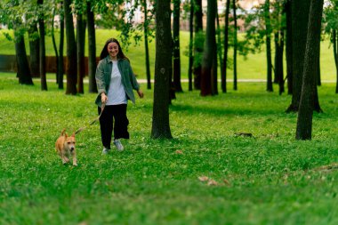 Küçük kırmızı köpek bakımı ve hayvanlara olan sevgisiyle parkta yürüyen genç bir kız.