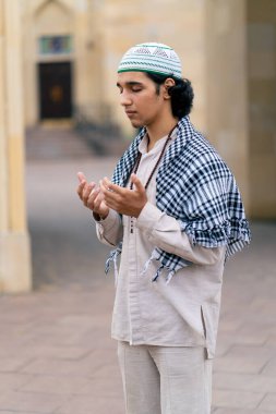 Ulusal giysiler içinde, boynunda tespihle cami avlusunda dua eden Arap bir adam.