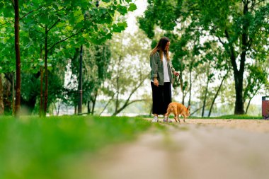 Küçük kırmızı köpek bakımı ve hayvanlara olan sevgisiyle parkta yürüyen genç bir kız.