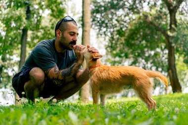 Parkta yürürken bıyıklı ve dövmeli vahşi bir adamın portresi köpeğiyle birlikte onu öper.