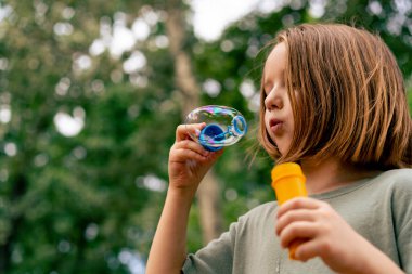 Şehir parkında sabun köpüğü üfleyen güzel küçük kız tasasız çocukluğu