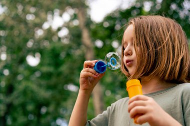 Şehir parkında sabun köpüğü üfleyen güzel küçük kız tasasız çocukluğu