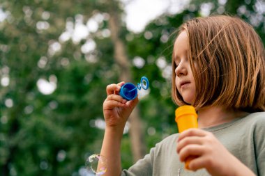 Şehir parkında sabun köpüğü üfleyen güzel küçük kız tasasız çocukluğu