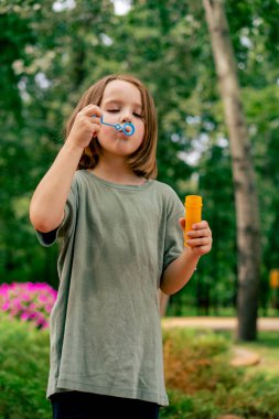 Şehir parkında sabun köpüğü şişiren güzel küçük kız portresi. Mutlu tasasız çocukluk.