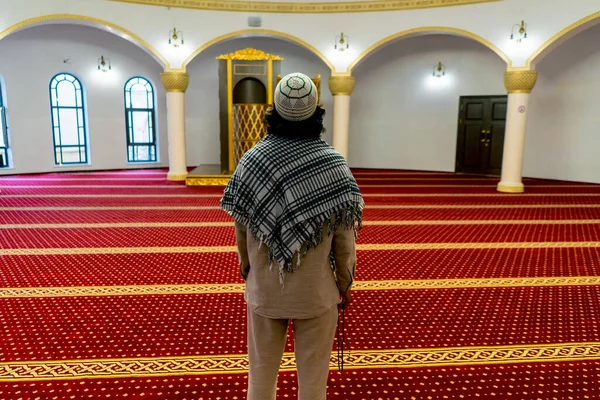 Shot from the back A Muslim man stands on the carpet in the middle of the prayer hall at the mosque with his head raised up