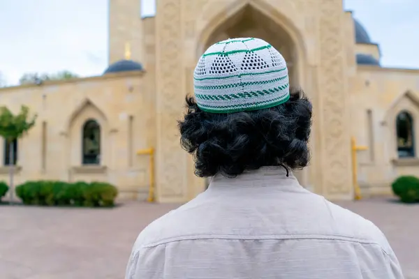 Back shot of a young Arab man entering the inner courtyard of a mosque on a terrace with Islamic ornamentation
