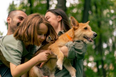 Parkta genç mutlu bir ailenin portresi. Köpek babası kızını kucağında tutuyor. Güven ve aile değerleri kavramında.
