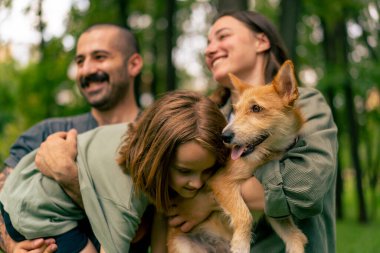 Parkta genç mutlu bir ailenin portresi. Köpek babası kızını kucağında tutuyor. Güven ve aile değerleri kavramında.