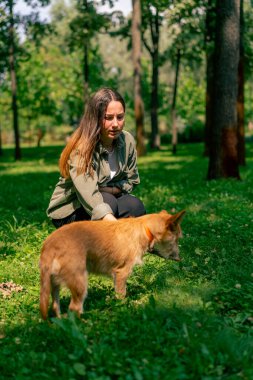 Parkta köpeğiyle yürüyen, sopayla oynayan ve onunla dalga geçen genç bir kızın portresi.