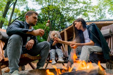 Şirin, genç bir aile babası, anne ve kızı ormanda bir ateşin başında oturmuş, kır evlerinin yanında şekerleme kızartıyorlar.