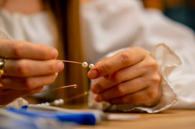 Kolye hobisi için bir tele kendi elleriyle boncuk takan genç bir kızın yakın çekim elleri.