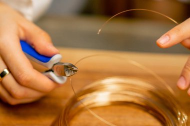 Kendi elleriyle mücevher yapan genç bir kızın elleri pense yapımında kullanılan kolye için tel kalıntılarını kesiyor.