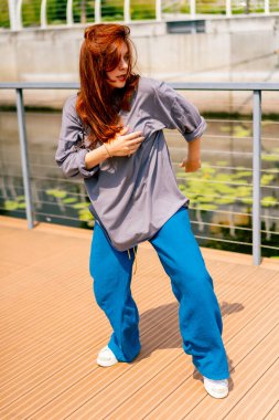 Genç, kızıl saçlı sokak hip-hop dansçısı spor kıyafetleri içinde doğaçlama danslar yapıyor. Bize briç oynuyor. Yoldan geçenlerin ilgisini çekiyor.
