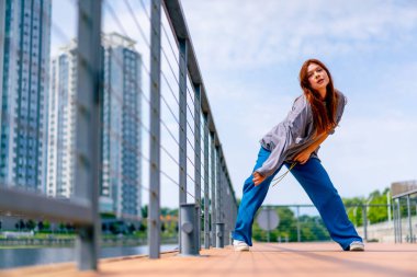Genç, kızıl saçlı sokak hip-hop dansçısı spor kıyafetleri içinde doğaçlama danslar yapıyor. Bize briç oynuyor. Yoldan geçenlerin ilgisini çekiyor.
