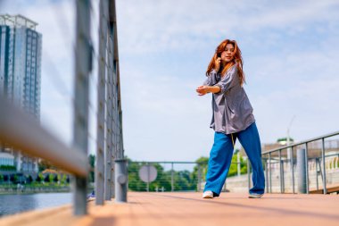 Genç, kızıl saçlı sokak hip-hop dansçısı spor kıyafetleri içinde doğaçlama danslar yapıyor. Bize briç oynuyor. Yoldan geçenlerin ilgisini çekiyor.