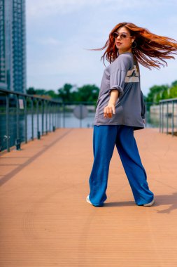 Genç, kızıl saçlı sokak hip-hop dansçısı spor kıyafetleri içinde doğaçlama danslar yapıyor. Bize briç oynuyor. Yoldan geçenlerin ilgisini çekiyor.