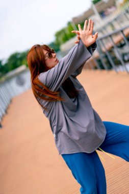 Genç, kızıl saçlı sokak hip-hop dansçısı spor kıyafetleri içinde doğaçlama danslar yapıyor. Bize briç oynuyor. Yoldan geçenlerin ilgisini çekiyor.