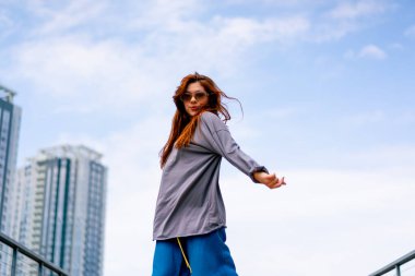 Genç, kızıl saçlı sokak hip-hop dansçısı spor kıyafetleri içinde doğaçlama danslar yapıyor. Bize briç oynuyor. Yoldan geçenlerin ilgisini çekiyor.