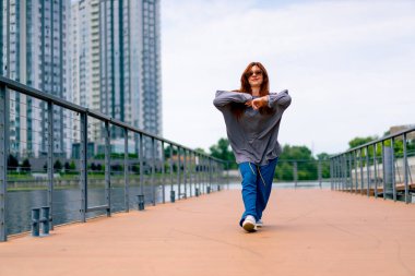 Genç, kızıl saçlı sokak hip-hop dansçısı spor kıyafetleri içinde doğaçlama danslar yapıyor. Bize briç oynuyor. Yoldan geçenlerin ilgisini çekiyor.