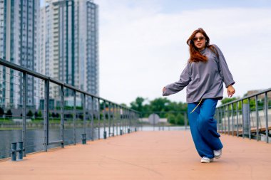 Genç, kızıl saçlı sokak hip-hop dansçısı spor kıyafetleri içinde doğaçlama danslar yapıyor. Bize briç oynuyor. Yoldan geçenlerin ilgisini çekiyor.