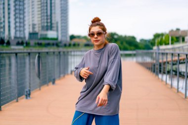 Genç, kızıl saçlı sokak hip-hop dansçısı spor kıyafetleri içinde doğaçlama danslar yapıyor. Bize briç oynuyor. Yoldan geçenlerin ilgisini çekiyor.