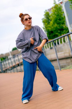Genç, kızıl saçlı sokak hip-hop dansçısı spor kıyafetleri içinde doğaçlama danslar yapıyor. Bize briç oynuyor. Yoldan geçenlerin ilgisini çekiyor.