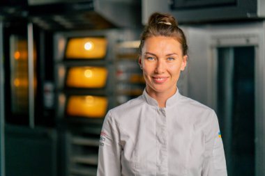 Fırının arka planında profesyonel üniformalı gülümseyen bir aşçı kadın fırının portresi ve taze pişmiş yiyecekler.